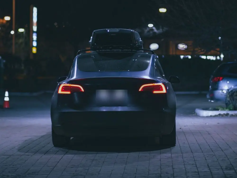 Tesla noire à l'arrêt de nuit, feux arrière allumés
